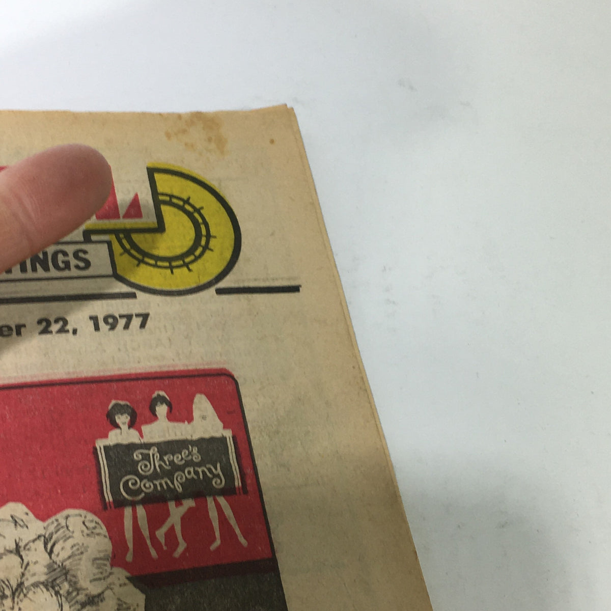 Close-up of the vintage magazine cover titled 'VTG TV Dial Complete Cable Listings October 15-22 1977 Three's Company on ABC', showing slight wear and a finger pointing at the top corner.