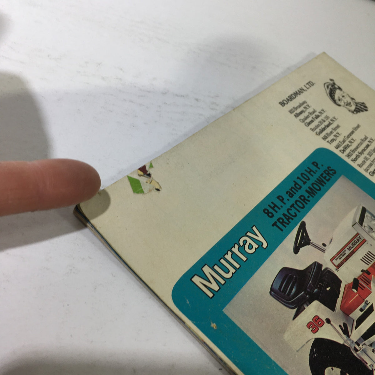 VTG Boardman Ltd. Price Guide Catalog Spring & Summer 1976 Super Scramper highlighting the corner of the Murray tractor mower advertisement, with finger pointing towards minor wear on the page.