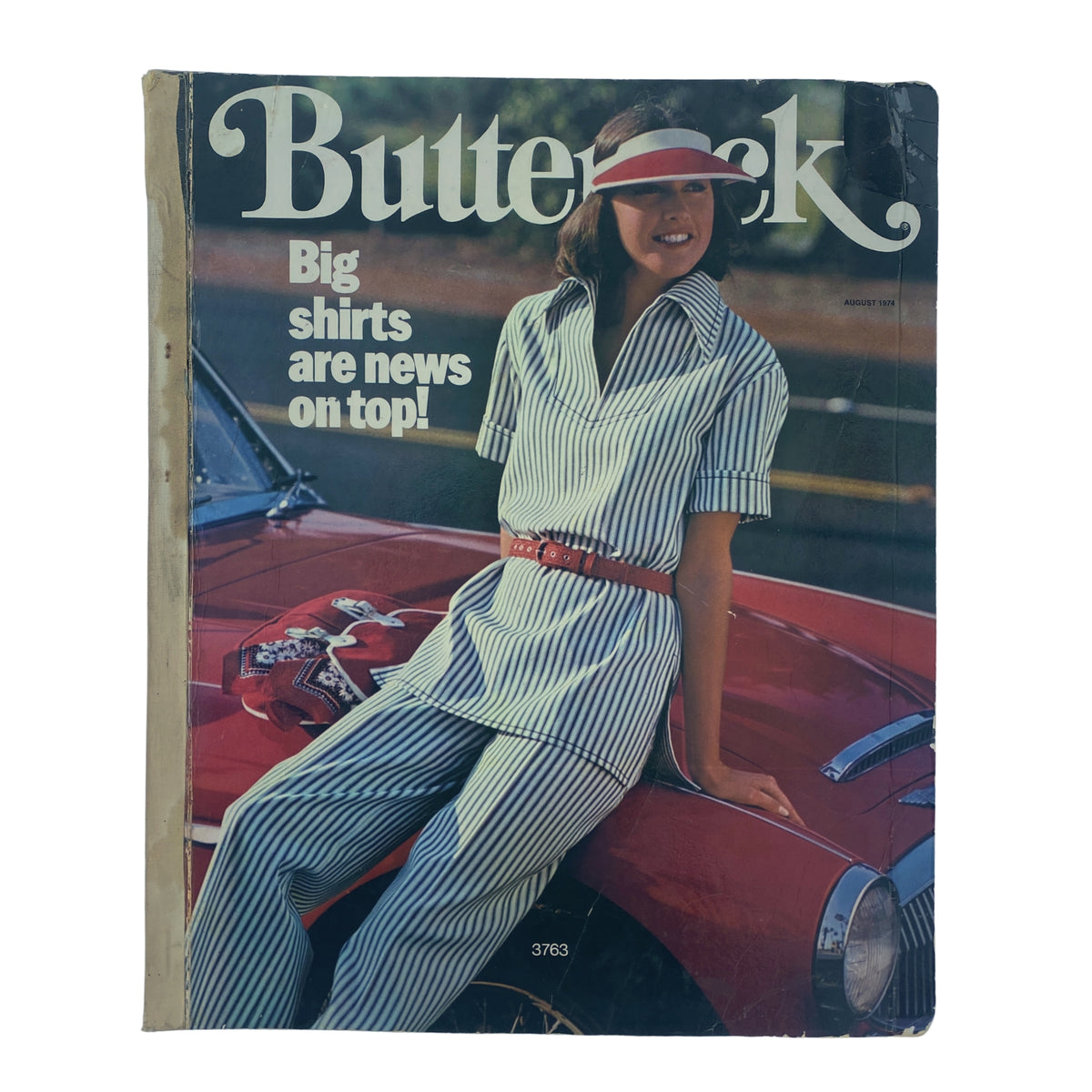 Cover of the 1974 August Butterick Catalog showcasing a model in a striped outfit, promoting large shirts, with a classic car in the background.