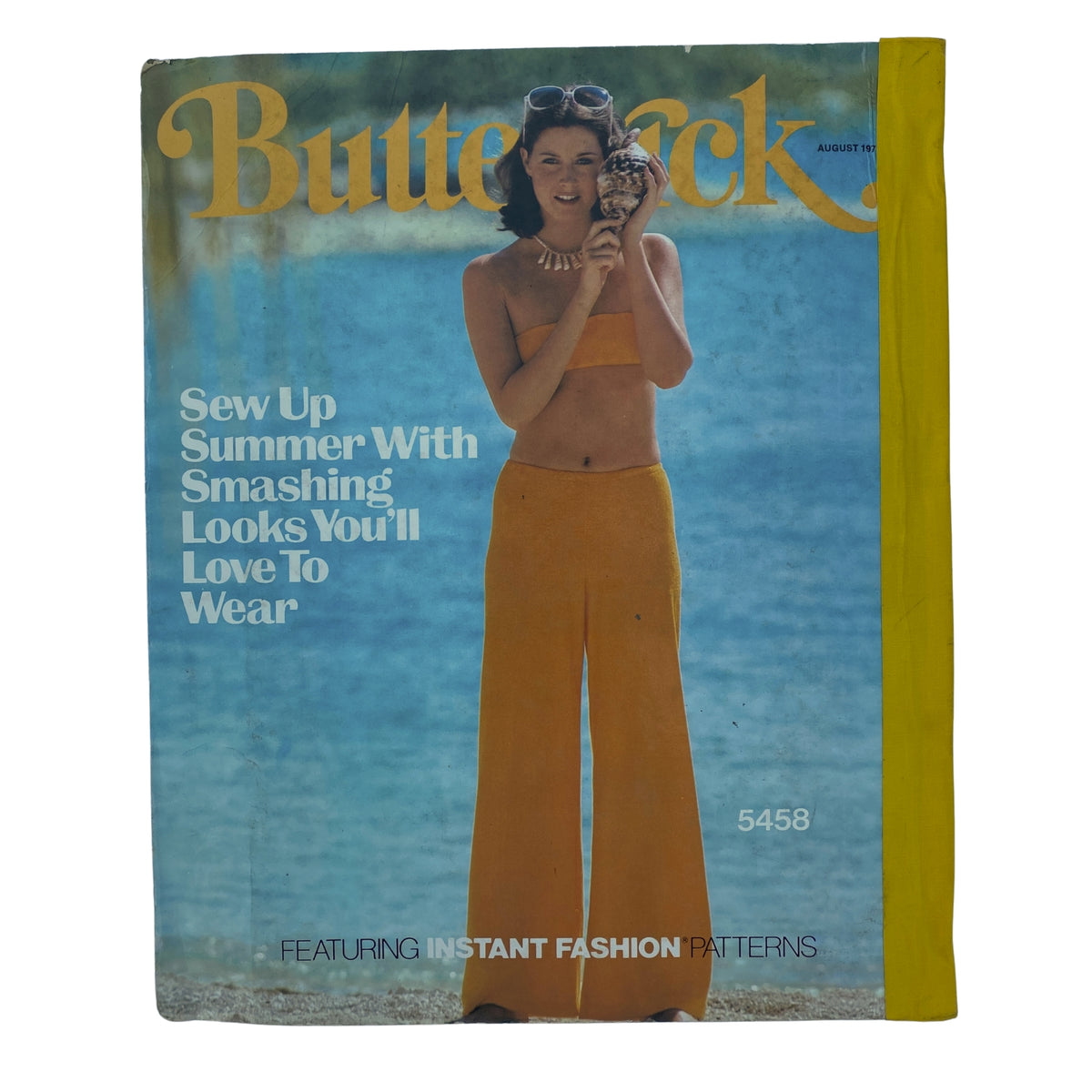 Cover of the 1977 August Butterick Catalog showcasing a model in a yellow two-piece outfit against a beach background, promoting summer sewing patterns.
