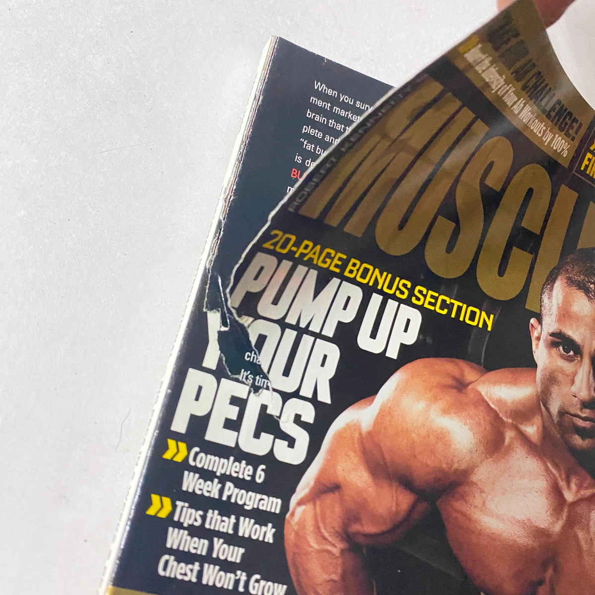 Close-up view of the MuscleMag Magazine March 2009 No. 322 cover with a tear, showcasing a bodybuilder and highlighting the theme 'Pump Up Your Pecs' along with fitness insights.
