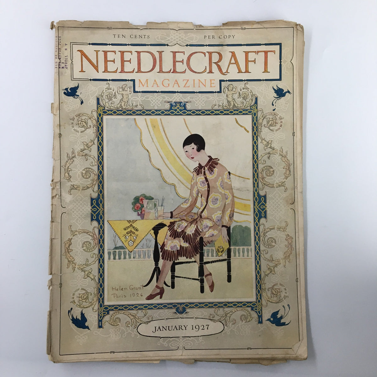 Cover of VTG Needlecraft Magazine January 1927 featuring an artistic illustration of a woman seated at a table, while highlighting the title and month.