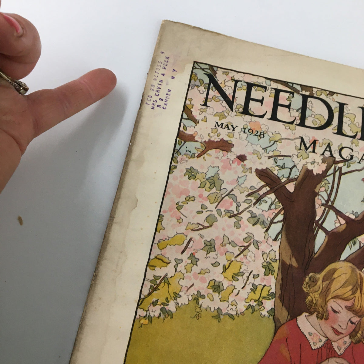 Cover of the VTG Needlecraft Magazine May 1928 Vol. 19 No. 9, featuring a woman under a flowering tree with soft pastel colors.