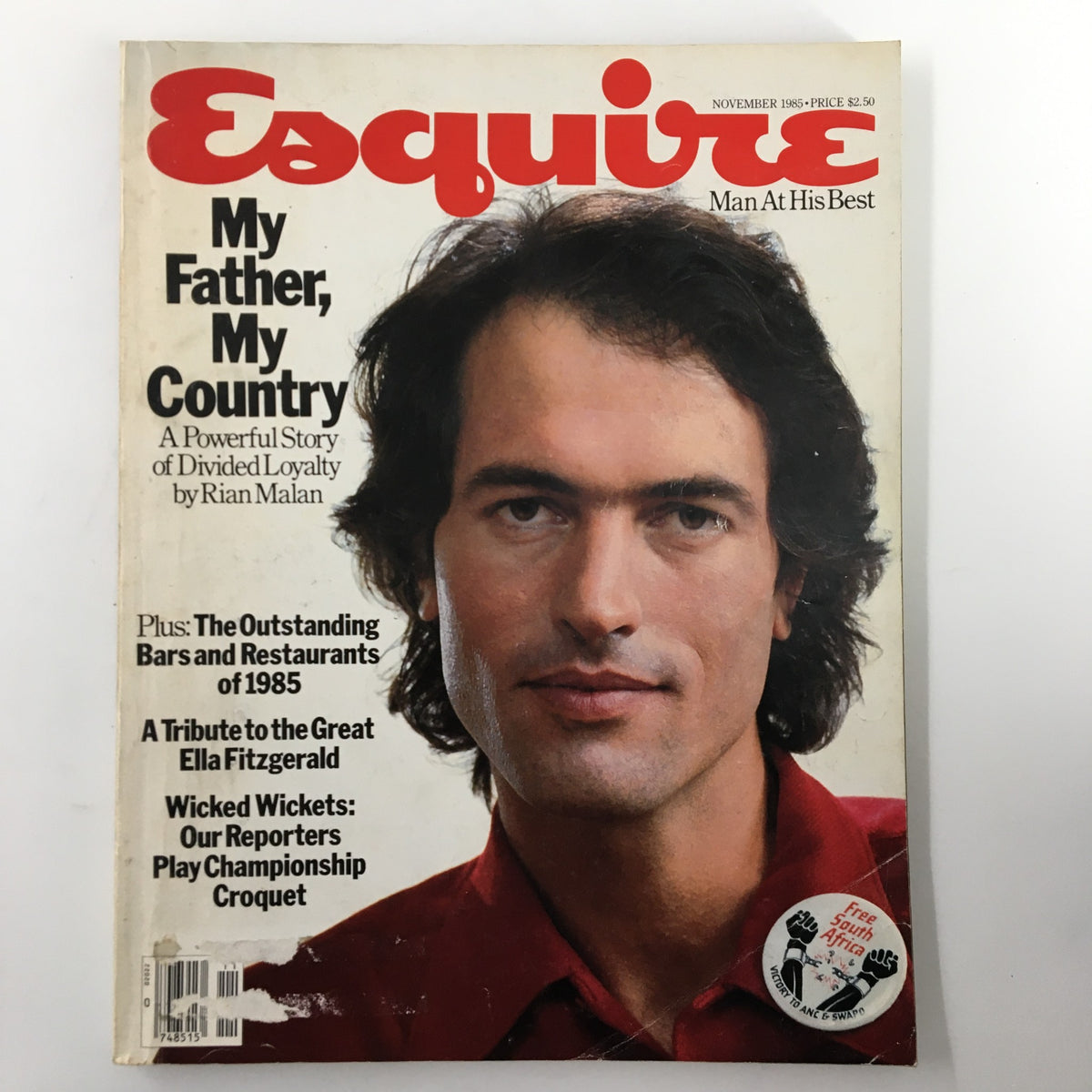 Esquire Magazine cover from November 1985 featuring the title 'My Father, My Country' and the tagline 'A Powerful Story of Divided Loyalty.' The cover showcases a male model with dark hair and a red shirt, along with highlights on features like bars and restaurants of 1985, a tribute to Ella Fitzgerald, and a badge reading 'free South Africa.'