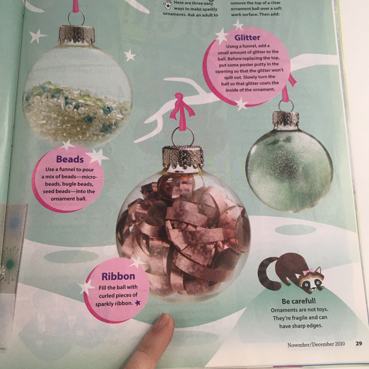 Craft ideas featured in American Girl Magazine November 2010, showcasing decorated ornaments using beads, glitter, and ribbon with a raccoon illustration.