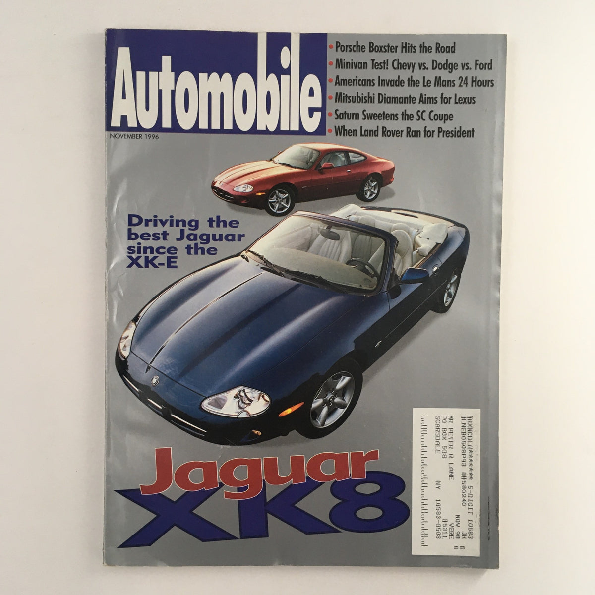 Cover of Automobile Magazine from November 1996 featuring the Jaguar XK8, with headlines about the Porsche Boxster, and several automotive topics. The image showcases a blue Jaguar XK8 convertible prominently displayed alongside a red car.