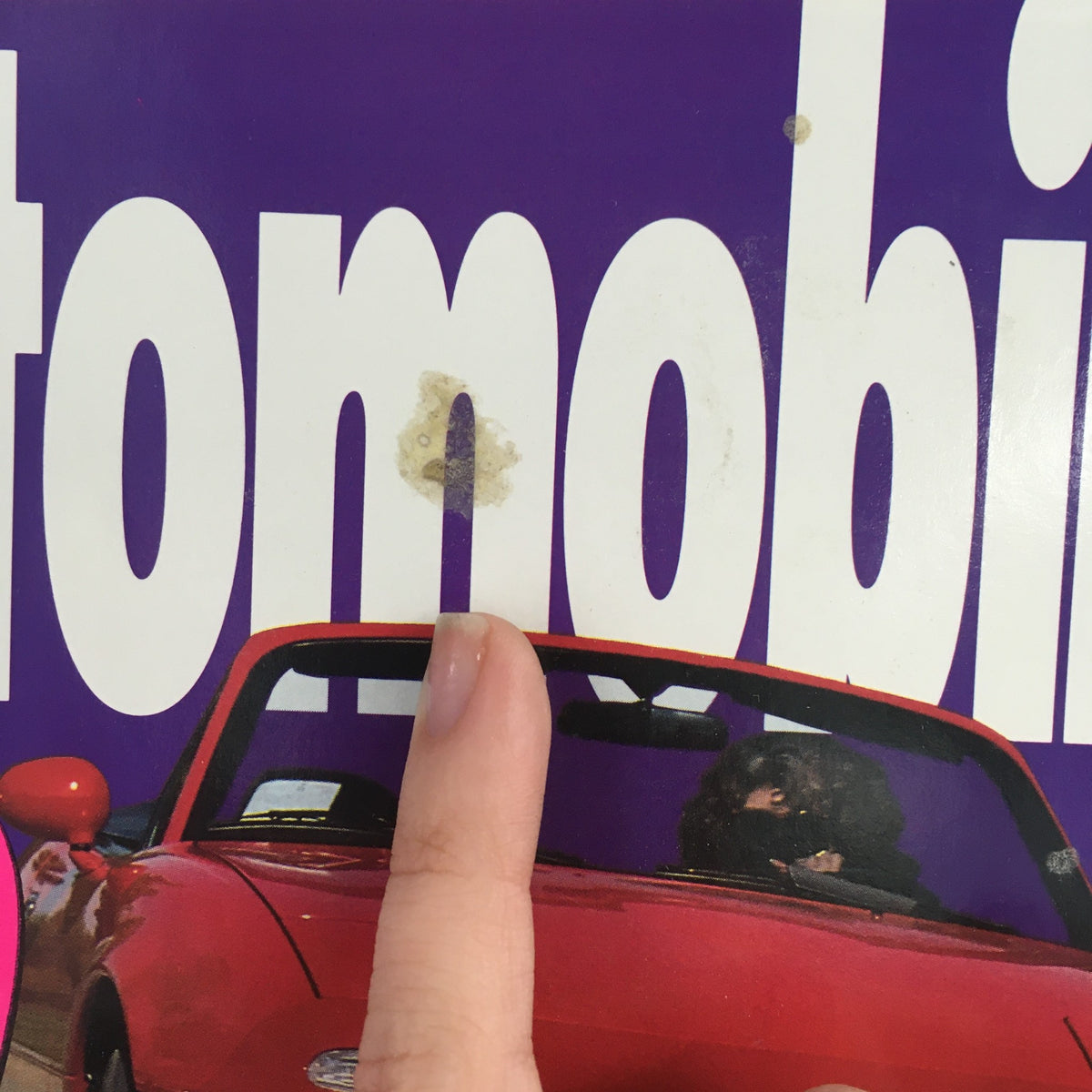 Close-up of the cover of Automobile Magazine, July 1994, showing a stain on the title with a finger pointing at it, featuring the Mazda Miata and advertising text.