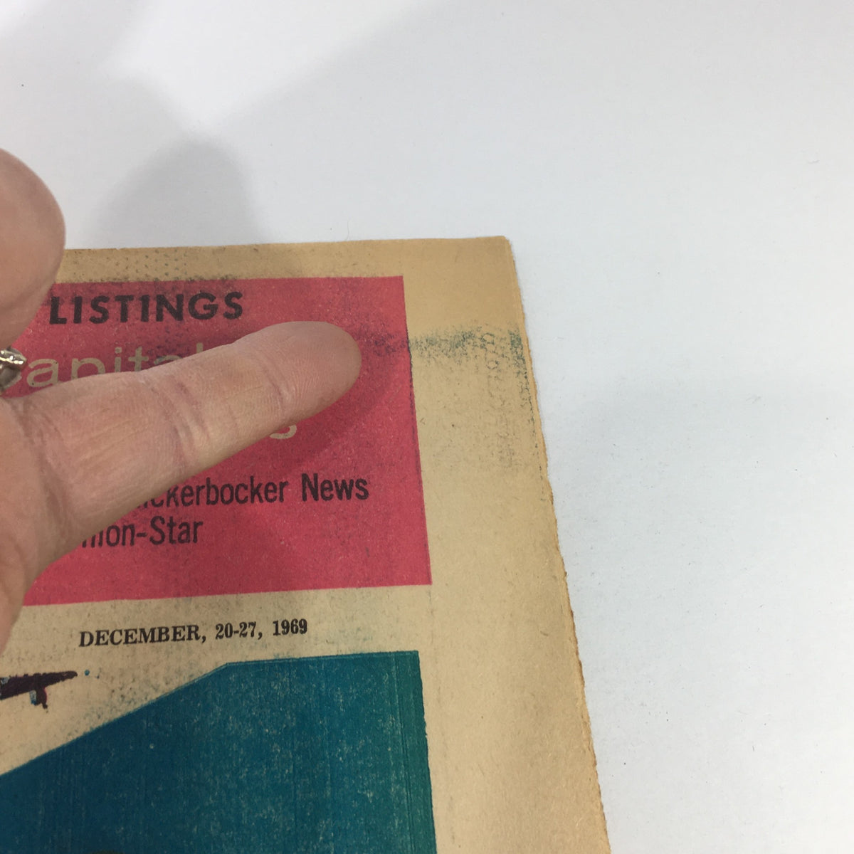 Close-up of the VTG TV Week's Complete TV Listings from December 20-27, 1969 showing a finger pointing at the cover highlighting 'Capital' and details about the magazine's origins from the Knickerbocker News.