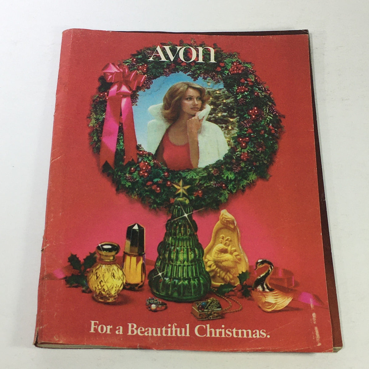 Cover of the VTG Avon Christmas Price Guide Product Catalog December 1974 featuring a woman surrounded by festive decorations and Avon products.
