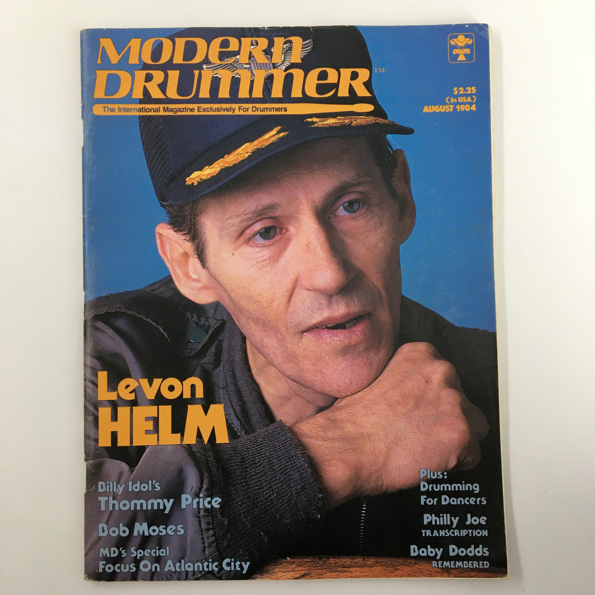 Cover of the August 1984 issue of Modern Drummer magazine featuring Levon Helm, a notable drummer, wearing a cap and showcasing his signature style. The magazine highlights drumming insights and interviews with prominent artists.