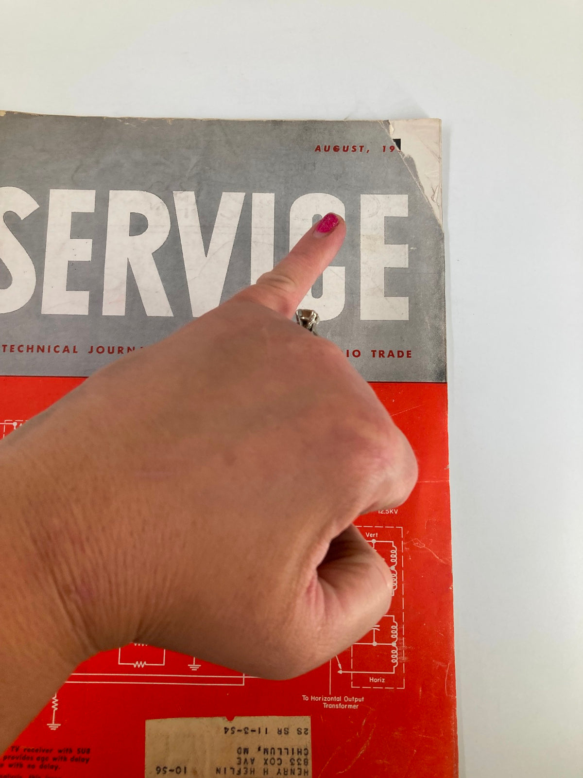 Close-up view of the cover of VTG Service Magazine August 1956, with finger pointing at the title, emphasizing the publication's technical content.