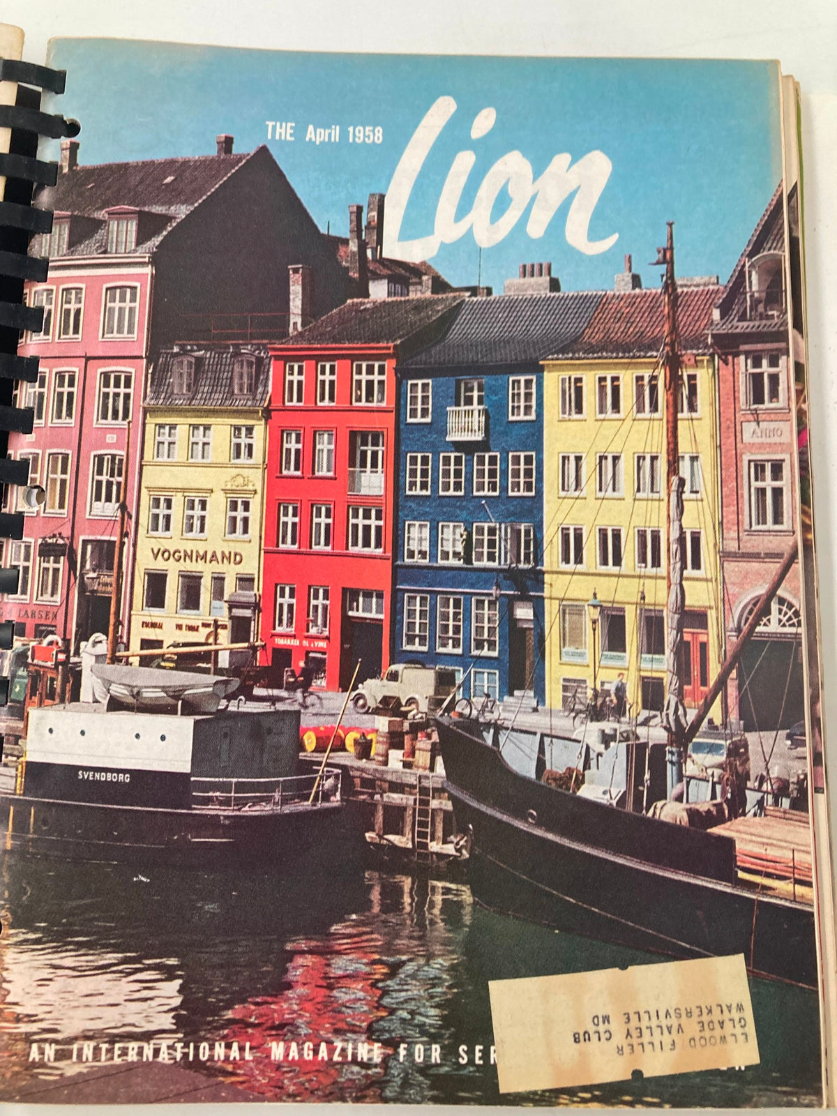 Cover of the April 1958 issue of The Lion Magazine illustrating colorful buildings by a waterfront, capturing the beauty of vintage design, a noteworthy addition for collectors.