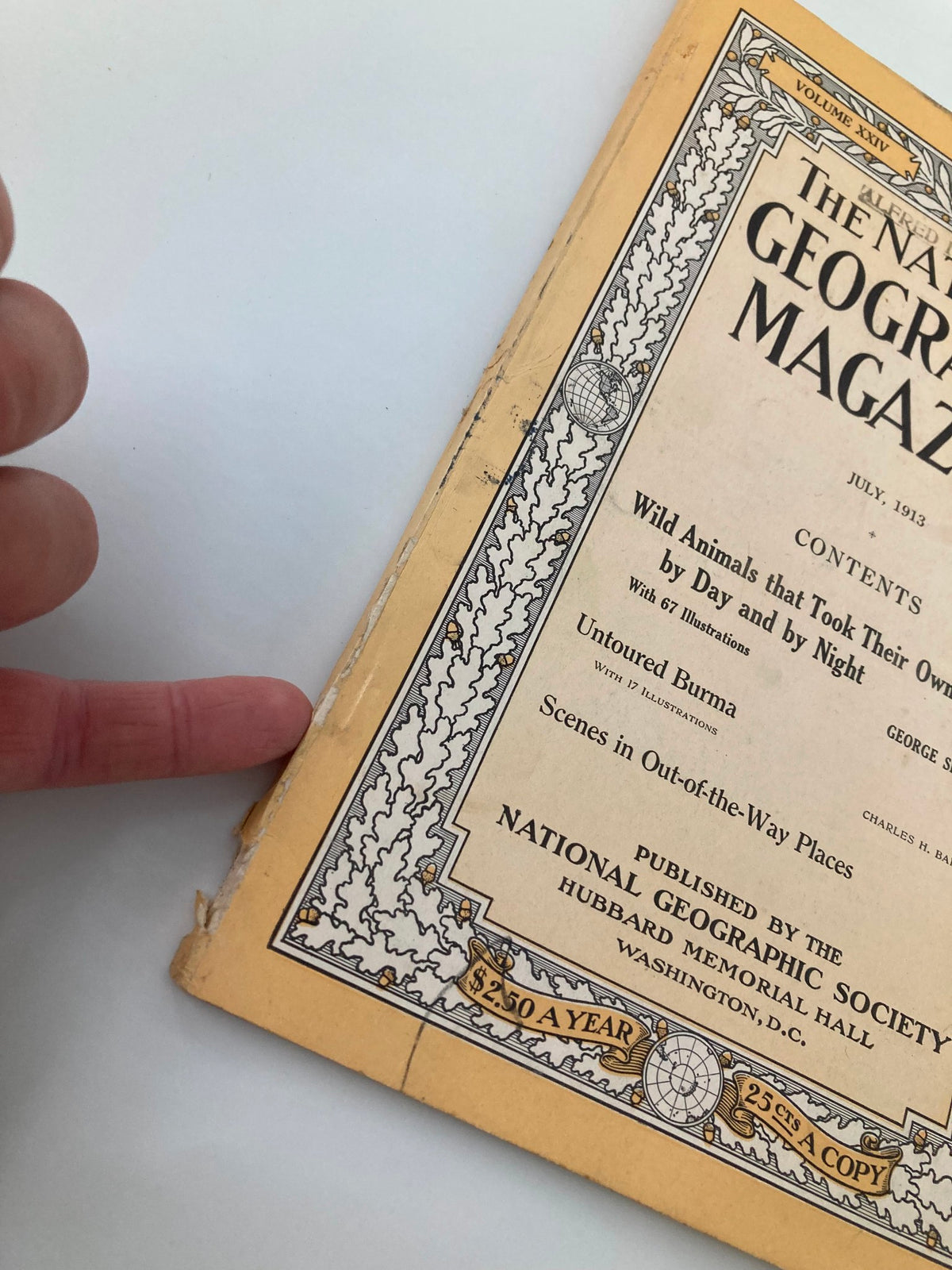 Close-up image of the spine of the July 1913 National Geographic Magazine, highlighting wear and features including a pointer finger indicating minor damage.