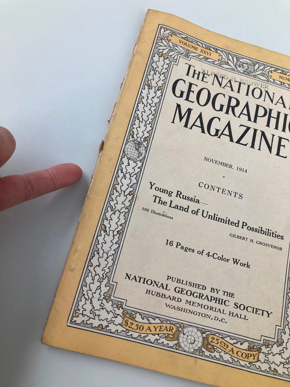 Close-up of the cover of the National Geographic Magazine, November 1914 edition, showcasing the title 'The Land of Unlimited Possibilities' with a finger pointing to the text.