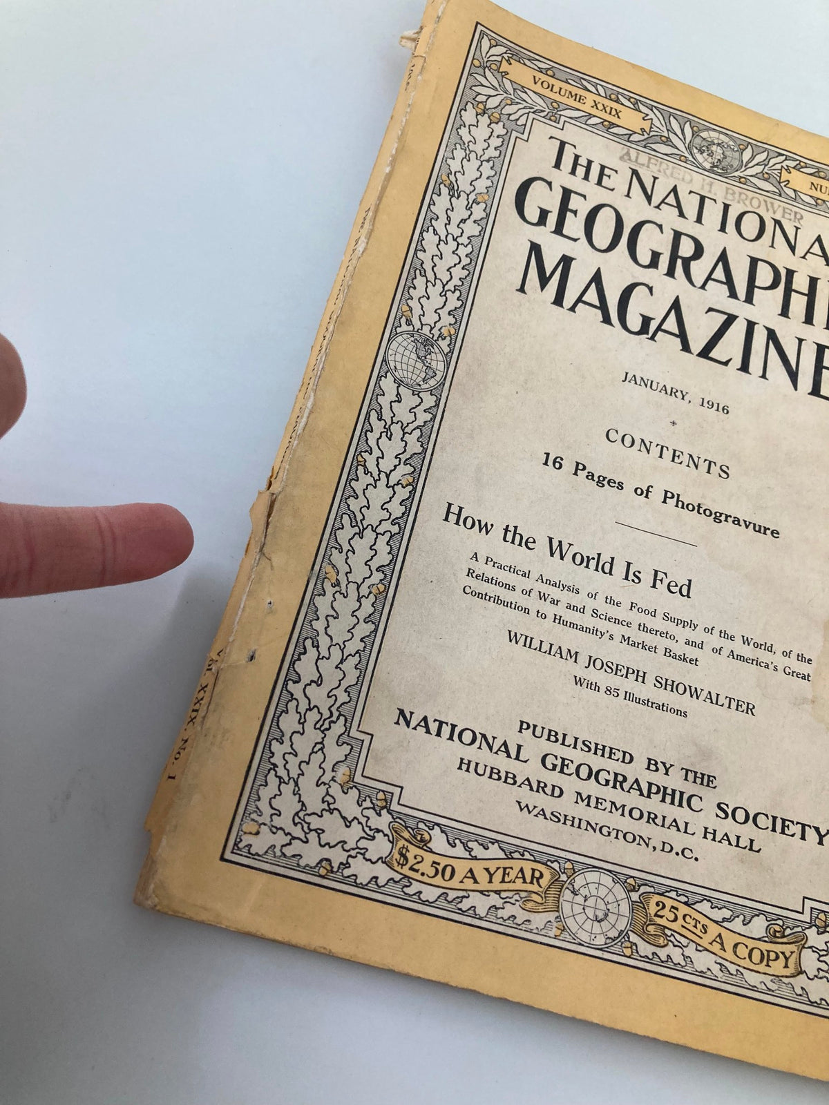 Detail of the January 1916 National Geographic Magazine cover, highlighting the title 'How The World is Fed' and a finger pointing to a corner of the page.