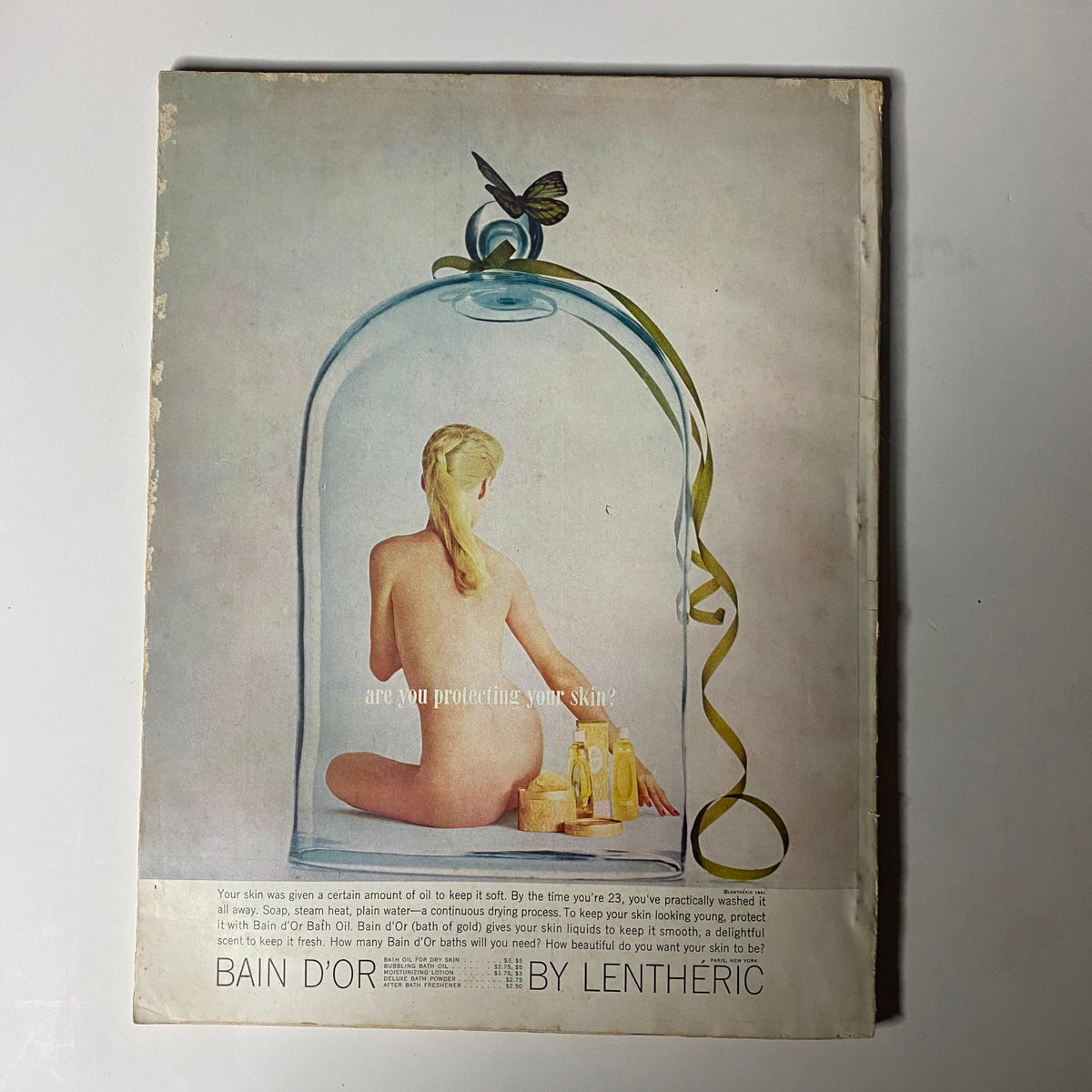 Back cover of Harper's Bazaar Magazine February 1962 featuring a vintage advertisement for body care products, using a creative image of a woman under a glass dome.