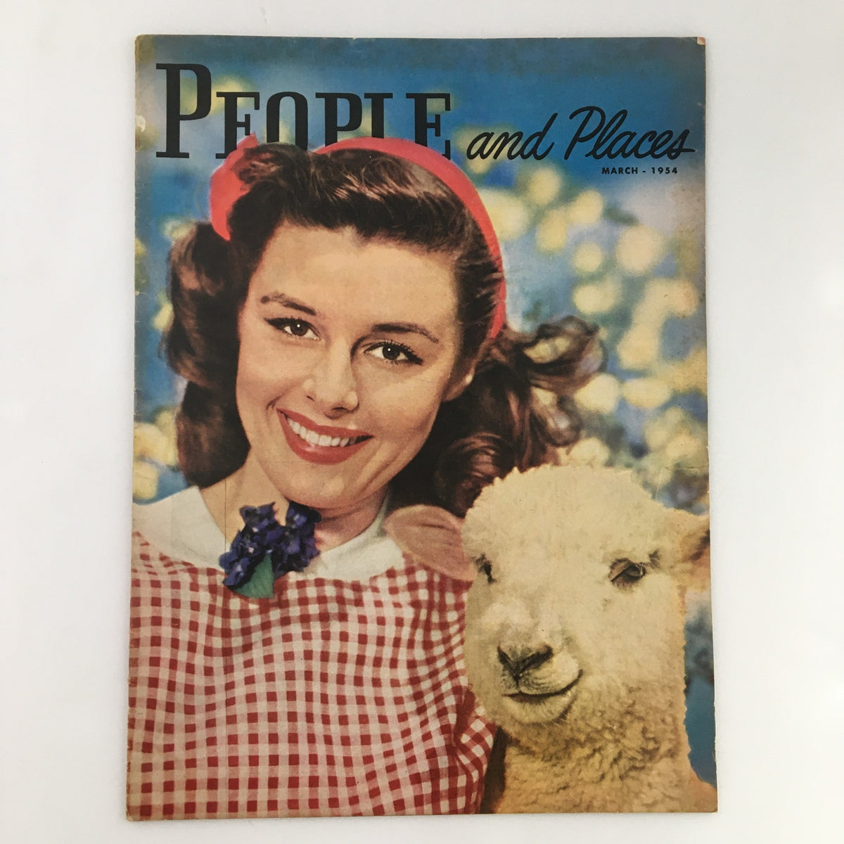 March 1954 People and Places Magazine cover featuring a smiling lady in a checkered outfit with a lamb, encapsulating vintage charm and nostalgia.