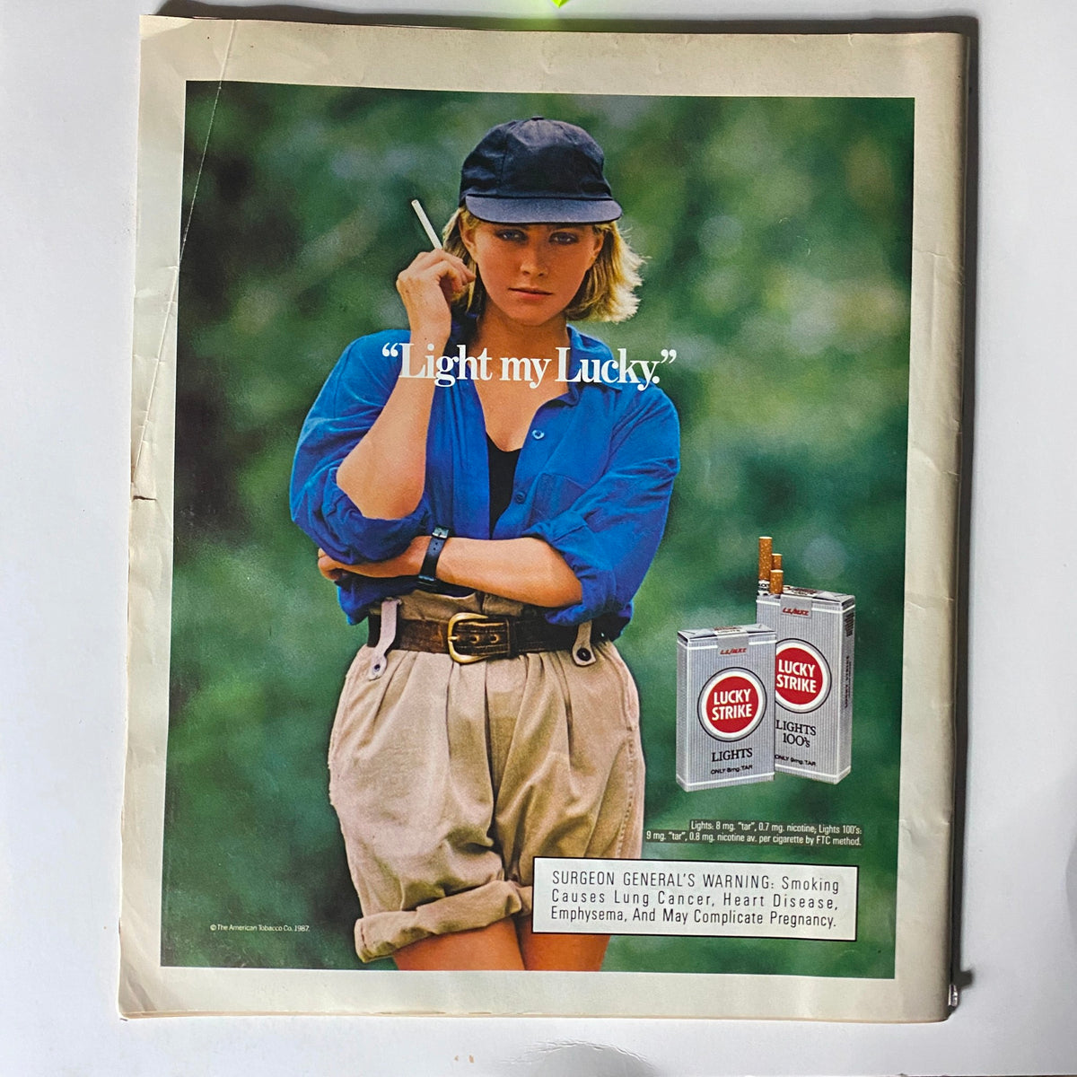 Vintage magazine advertisement from Spin Magazine August 1987 featuring a woman in a blue shirt and hat holding a cigarette with the text 'Light my Lucky.' The ad promotes Lucky Strike Lights cigarettes, highlighting the 1980s style and culture, which aligns with the collectible Spin Magazine, Vol 3 No. 5 that features Simple Minds and Little Steven.