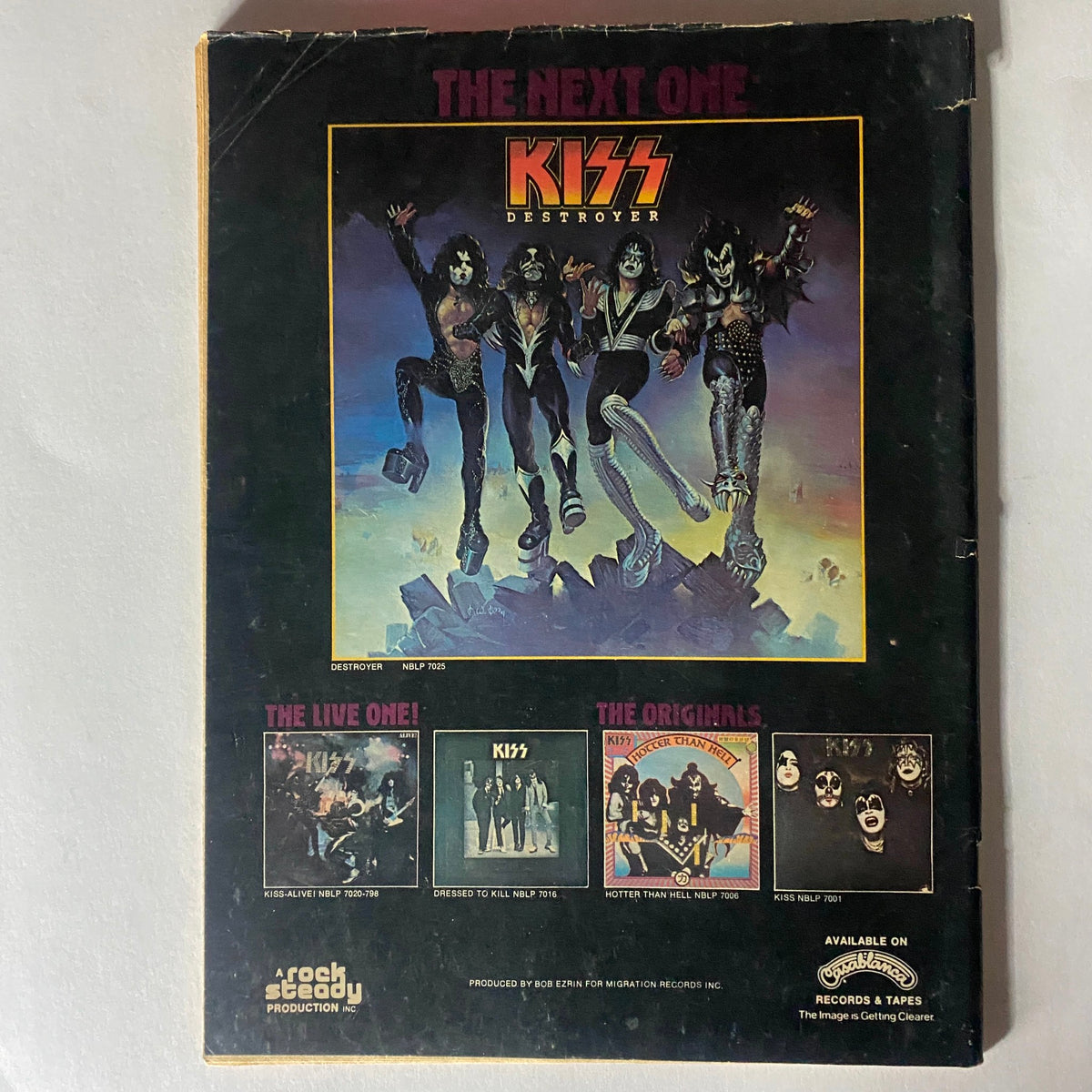 Back cover of the VTG Rock Scene Magazine from July 1976 featuring iconic rock band Kiss with promotional images of their albums, including 'Destroyer,' 'Alive,' 'Dressed to Kill,' and 'Hotter than Hell.' Includes text stating 'The Next One' and showcasing a vivid representation of the 1970s rock music scene.