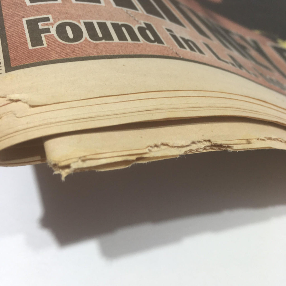 Close-up view of the edge of a vintage newspaper featuring the title 'New York Daily News: Feb 12 2012, Whitney Dead Found in L.A Hotel Room', highlighting worn edges and aged paper.