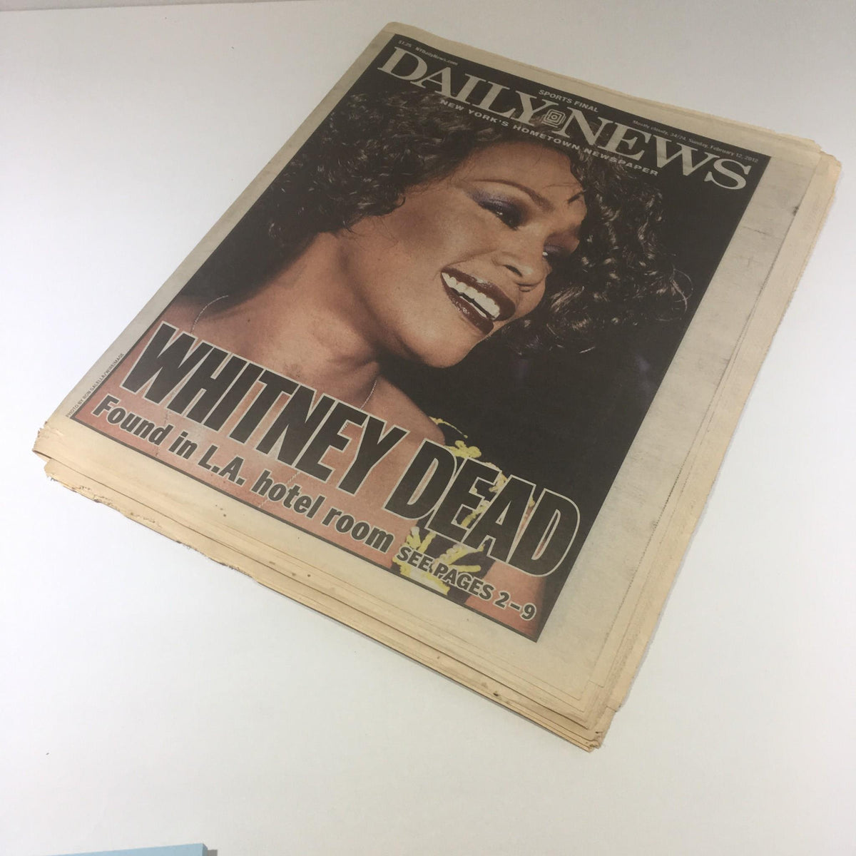 The front page of New York Daily News displaying the headline 'WHITNEY DEAD Found in L.A. hotel room', featuring a smiling portrait of Whitney Houston.