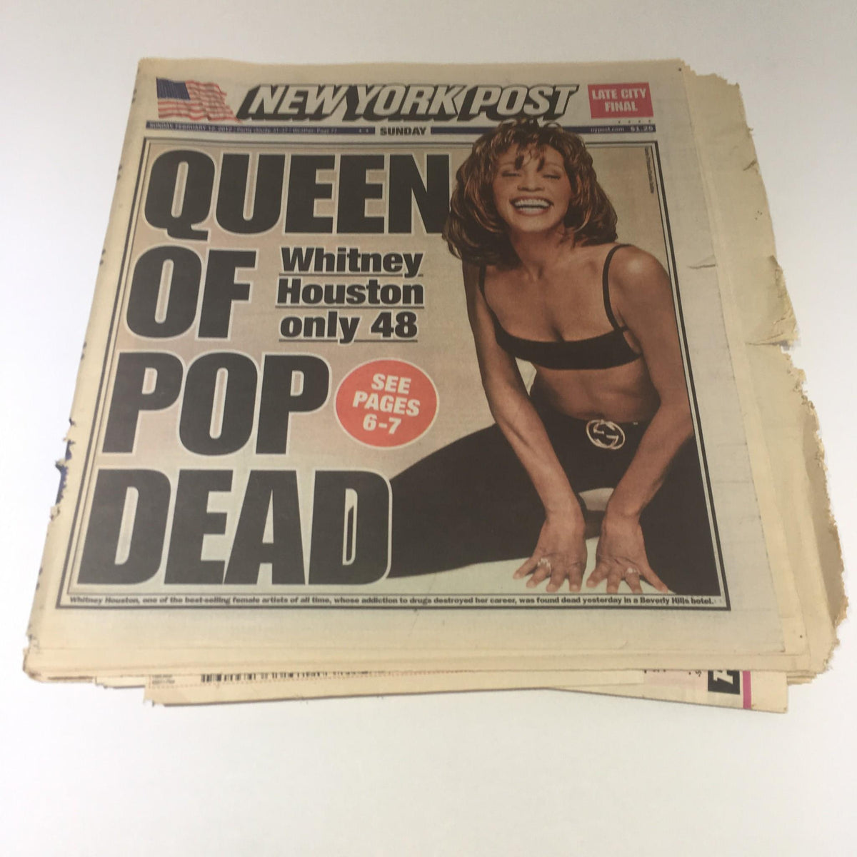 New York Post newspaper from February 12, 2012, featuring the headline 'Queen of Pop Dead' and an image of Whitney Houston. The newspaper highlights her age as 48 years.