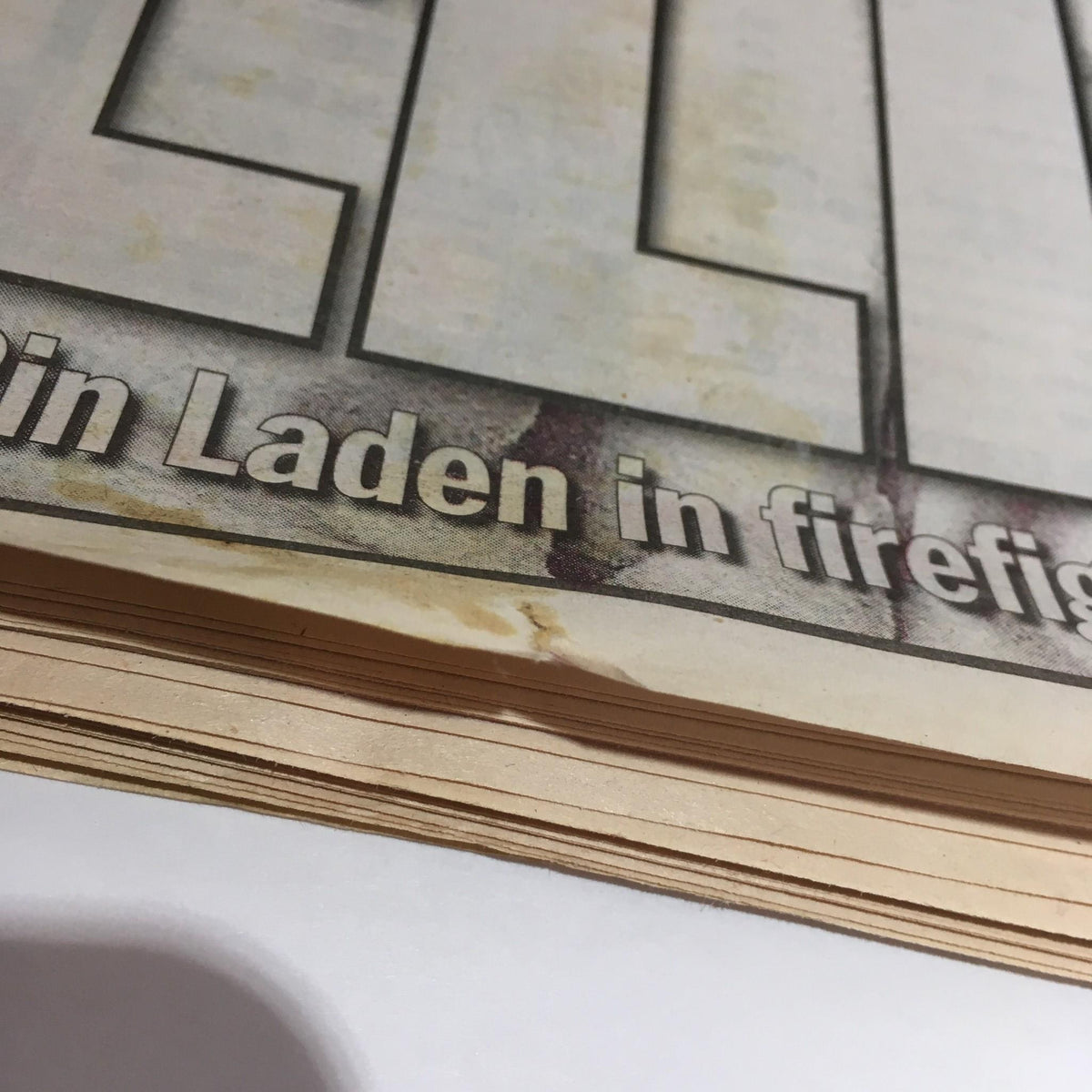 Close-up of the pages of NY Daily News dated May 2, 2011, highlighting minor wear and staining near the headline 'Rot in Hell! U.S. team kills Bin Laden in firefight'.