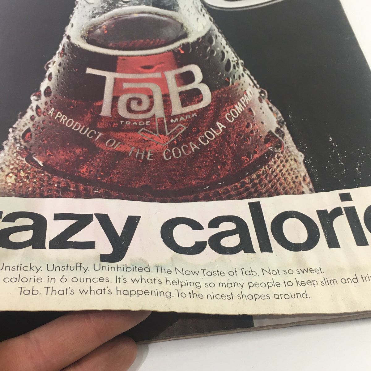 A close-up of a vintage advertisement featuring a Tab soda, showcasing its logo and the phrase 'crazy calories.' This ad highlights the product as a low-calorie option from Coca-Cola, making it a nostalgic piece related to the VTG The Saturday Evening Post April 9, 1966 - Stagecoach with Bing Crosby.