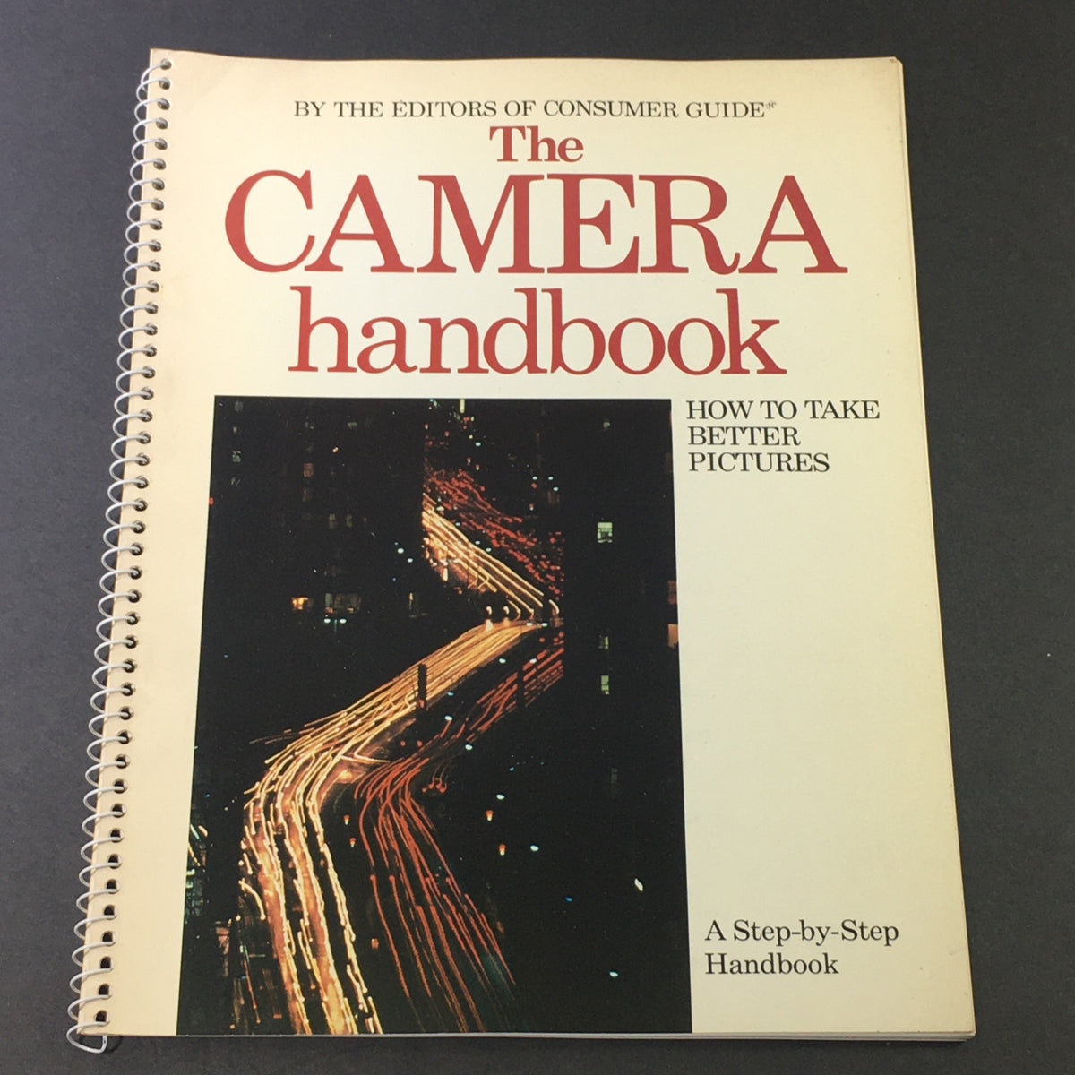 Cover of the 1982 The Camera Step-by-Step Handbook How To Take Better Pictures, featuring a colorful cityscape with lights at night and spiral binding.
