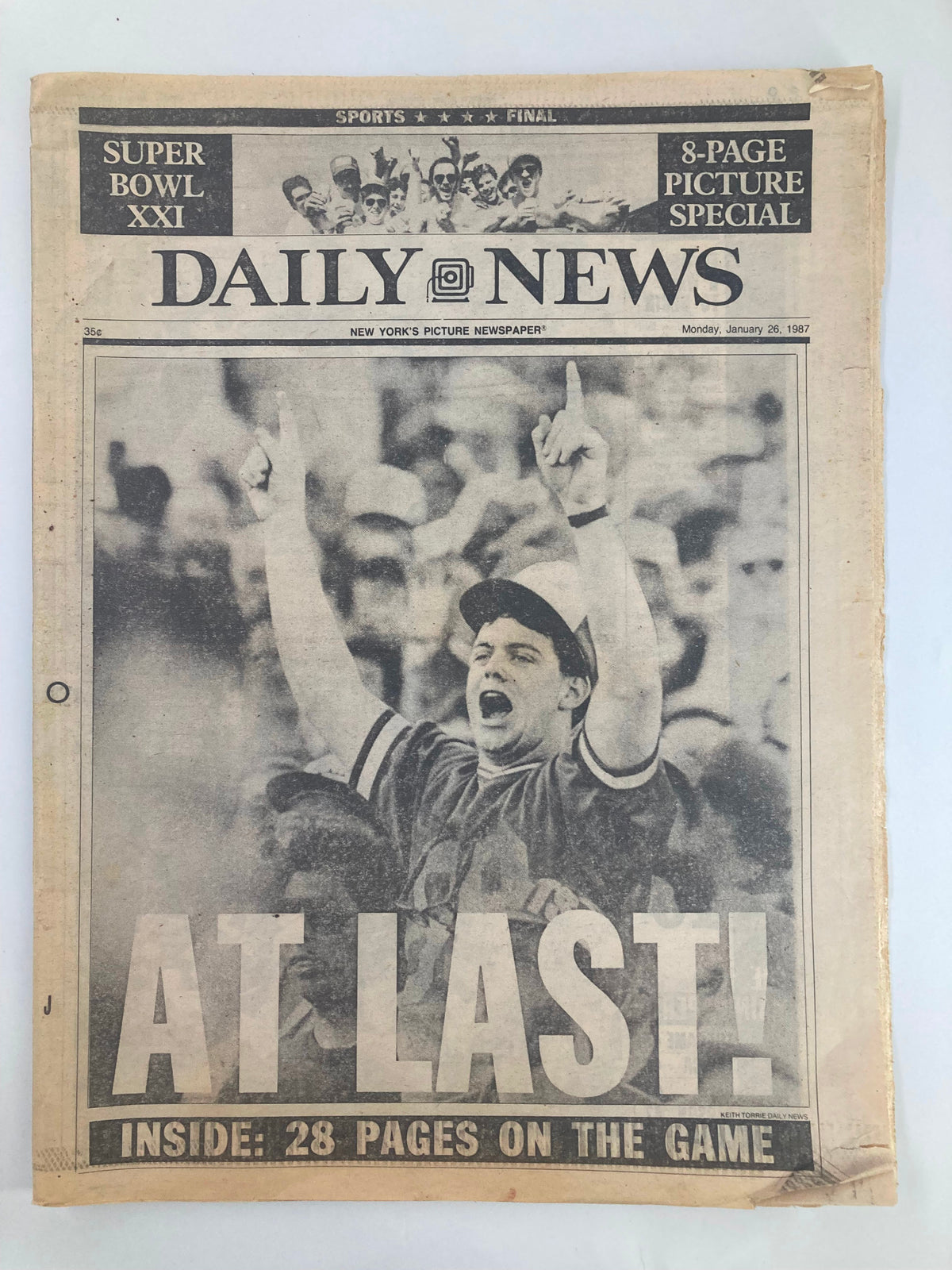 VTG Daily News Newspaper from January 26, 1987, featuring Coach Bill Parcells at Super Bowl XXI, showing an enthusiastic fan celebrating with raised arms in front of the newspaper headline 'AT LAST!'