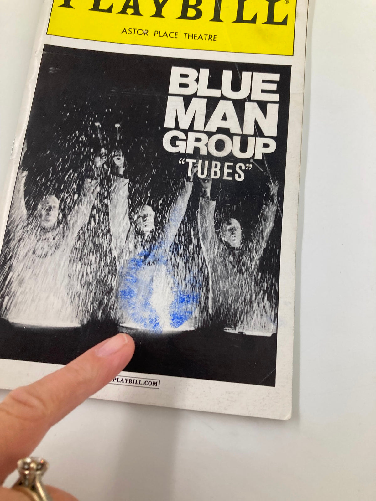 Close-up of the 2000 Playbill for Blue Man Group 'Tubes' at Astor Place Theatre, showcasing the performance and highlighting a finger pointing at the cover.