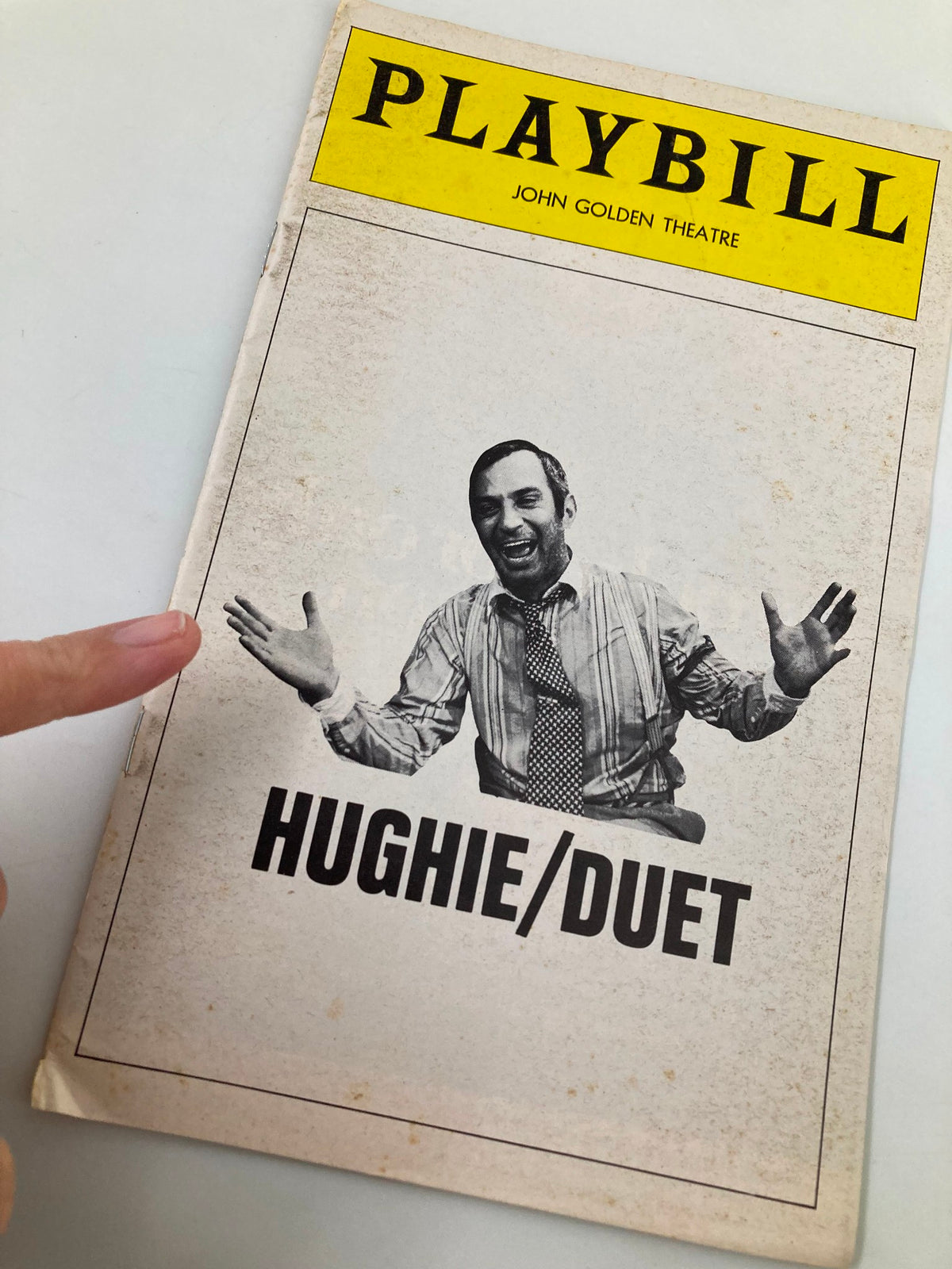 Close-up view of the 1975 Playbill for 'Hughie/Duet' at the John Golden Theatre with a finger pointing at the cover, highlighting the title and the featured character.