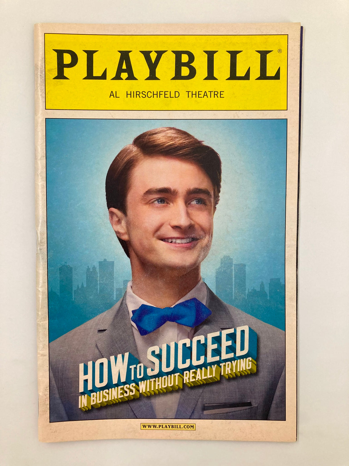 2011 Playbill for 'How To Succeed In Business Without Really Trying' featuring Daniel Radcliffe. The cover showcases a smiling Radcliffe in a suit and bow tie against a city skyline backdrop.