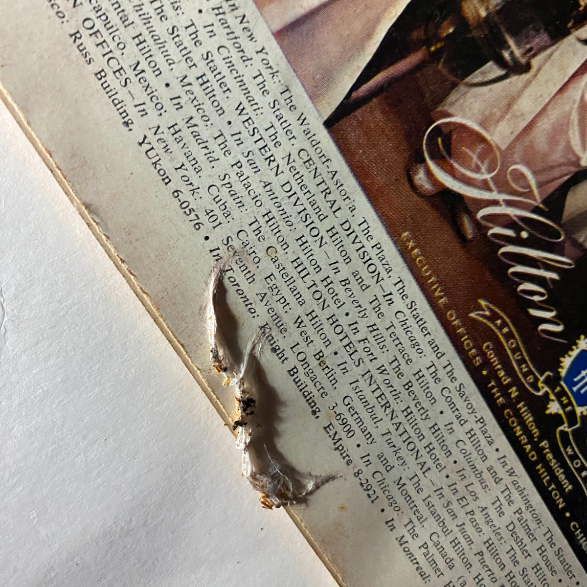 Close-up detail of the advertisement from VTG Time Magazine March 25, 1957 Vol 69 No. 12 for Hilton Hotels, showing a damaged corner. The ad emphasizes the luxury and entertainment available at various Hilton establishments.