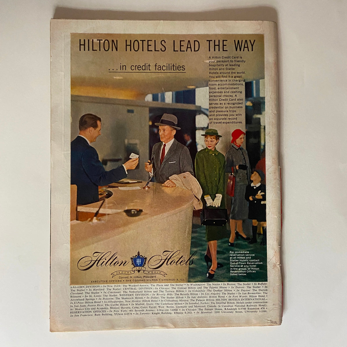 Vintage advertisement showcasing Hilton Hotels from Time Magazine, October 1, 1956, Vol 68 No. 14 featuring a man at a reception desk with guests, highlighting credit facilities in a stylish mid-century setting.