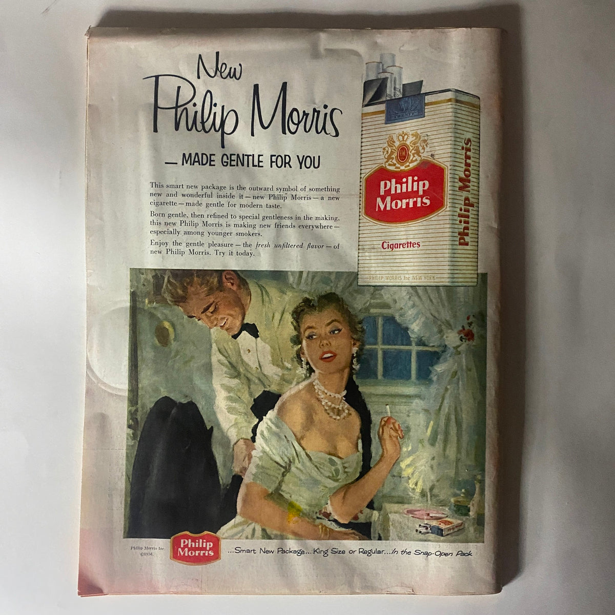 Advertisement for Philip Morris cigarettes featured in VTG Time Magazine January 16, 1956, showcasing a stylish couple, with a focus on the new packaging and gentle flavor of the cigarettes.