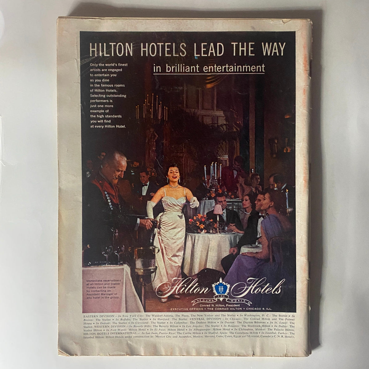 Advertisement page from Vintage Time Magazine April 16, 1956 promoting Hilton Hotels with an illustration of elegant dining and entertainment.