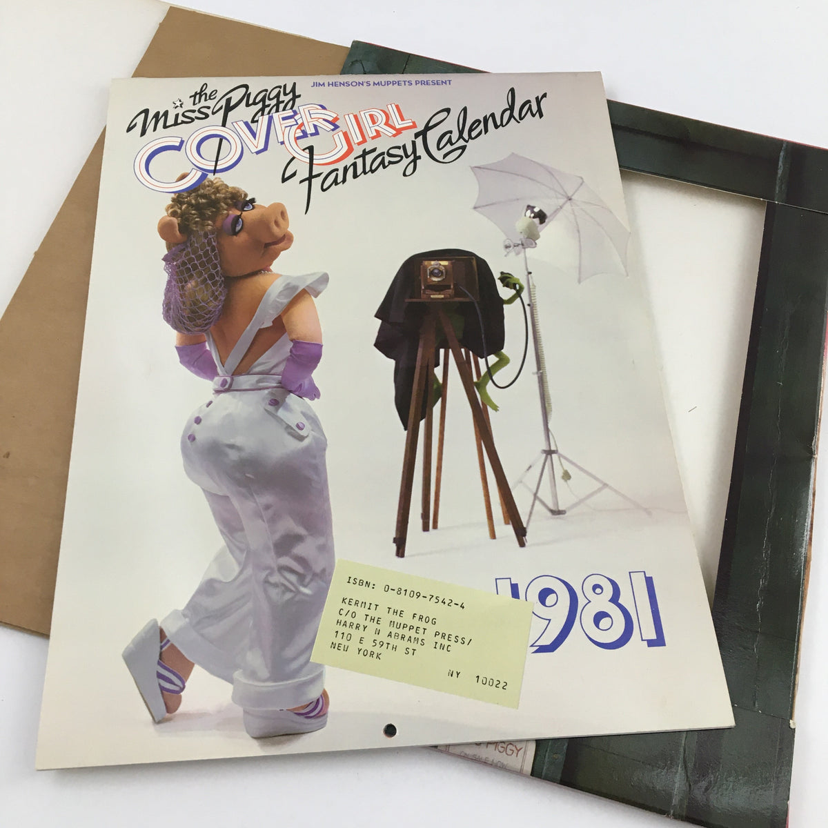 Back cover of Jim Henson's Muppets Present The Miss Piggy Cover Girl Fantasy Calendar 1981 showing Miss Piggy in a photography setting, wearing an elegant outfit and stylish accessories, emphasizing the playful nature of the Muppets.