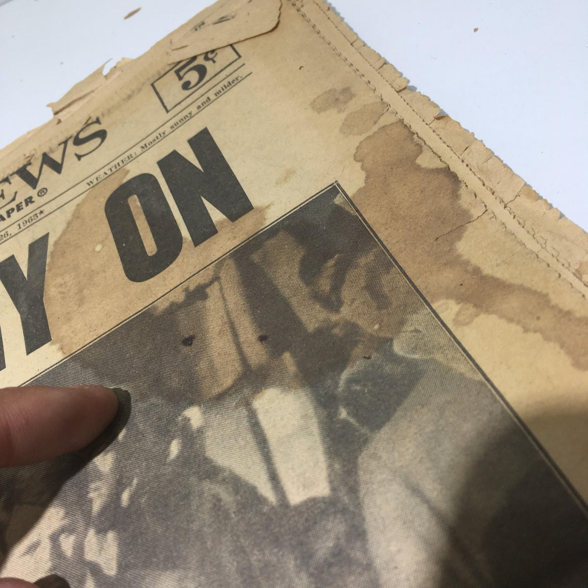 Close-up view of a vintage New York Daily News from November 26, 1963, titled 'We Carry On' featuring water stains and damage on the newspaper.