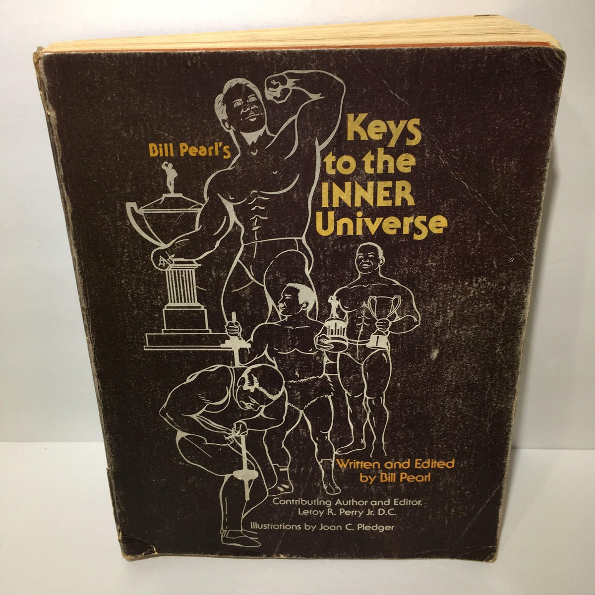 A close-up of the cover of 'Keys to the Inner Universe Vol. 1 1980 Third Printing by Bill Pearl' featuring illustrations of bodybuilders alongside the title.