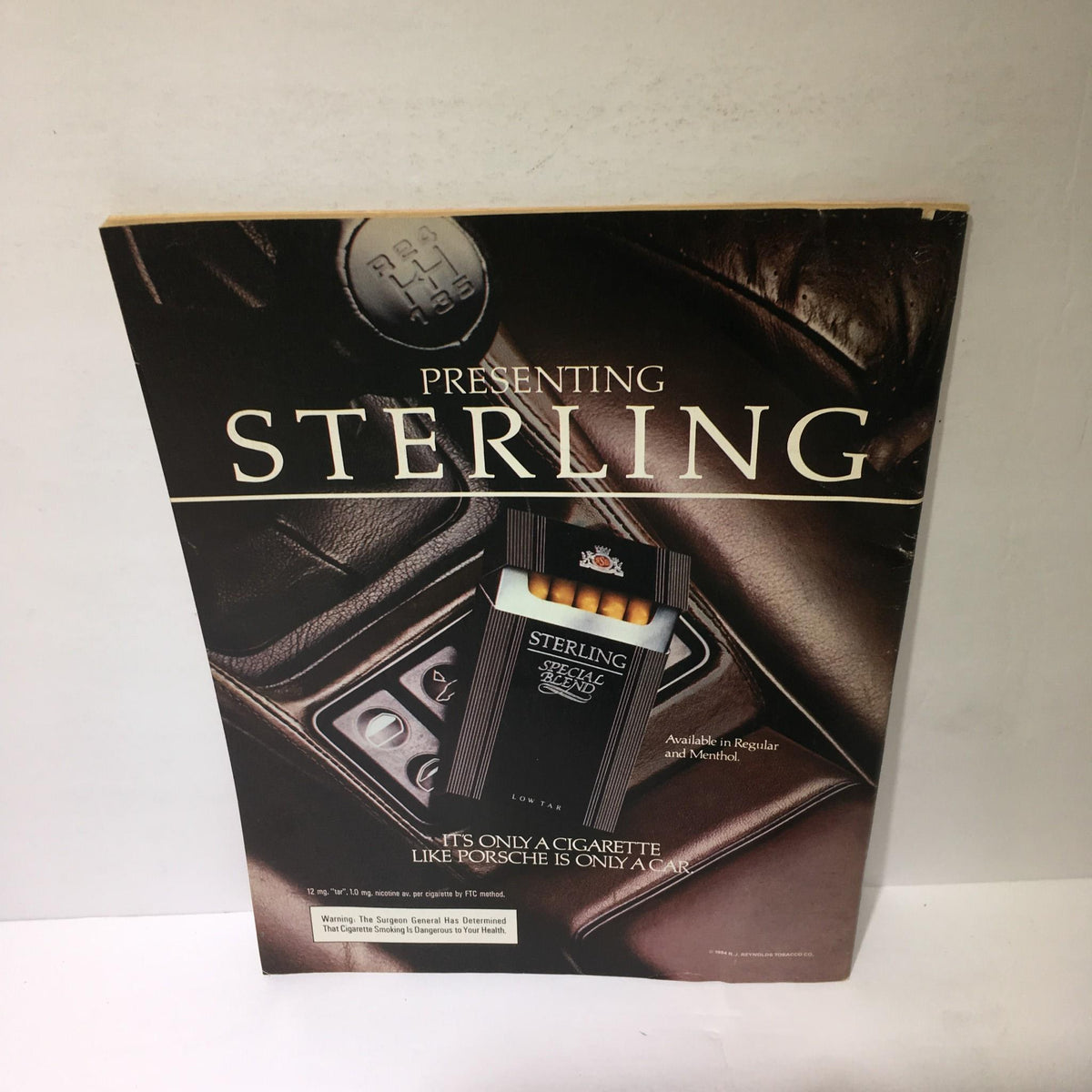 Image of an advertisement for Sterling cigarettes, showcasing the product with a luxury car backdrop, emphasizing the brand presentation.