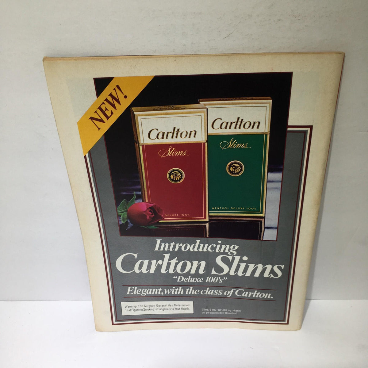 Advertisement for Carlton Slims Deluxe 100's cigarettes featured in a magazine, showcasing elegant packaging and a rose, with reference to the 1984 issue of Time titled "America's Banks Awash in Trouble."