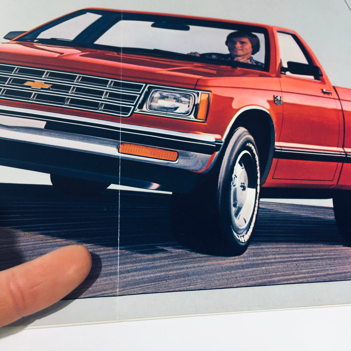 Front view of a red Chevy S-10 with a driver inside from the September 1981/4099 Chevy Trucks S-10 Tahoe Durango Sport Car Catalog Brochure, showcasing the vehicle's design and features.