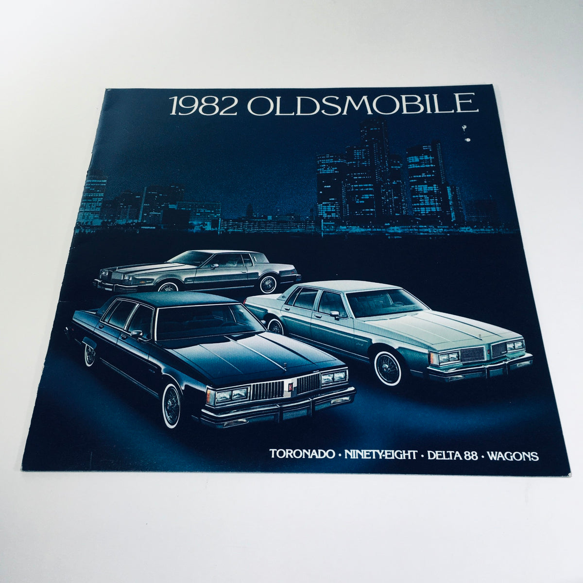 Cover of the 1982 Oldsmobile Tornado Ninety-Eight Delta 88 Wagons Car Sales Brochure featuring images of the cars and a city skyline background.