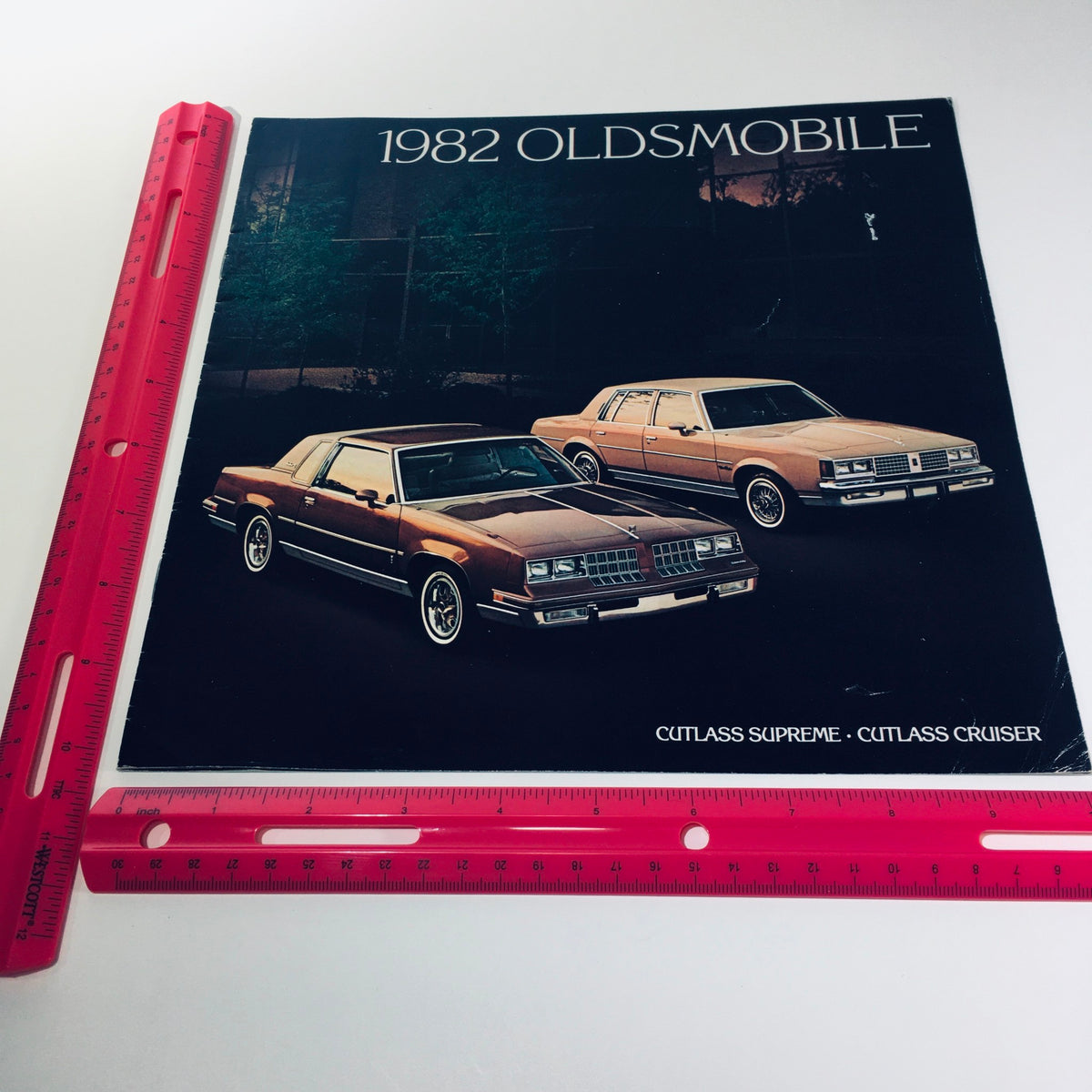 Front cover of the 1982 Oldsmobile Cutlass Supreme & Cutlass Cruiser sales brochure, displaying the two iconic cars and their stylish design, with a ruler for size reference.