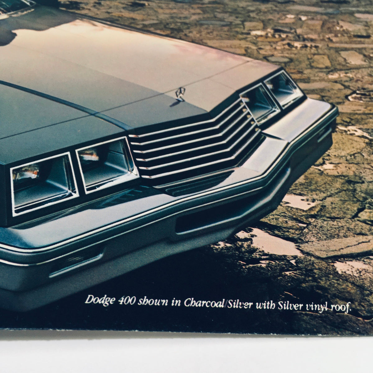 Close-up of the front of a 1982 Dodge 400 shown in Charcoal Silver with Silver vinyl roof, featuring distinctive design elements from the original car sale brochure.
