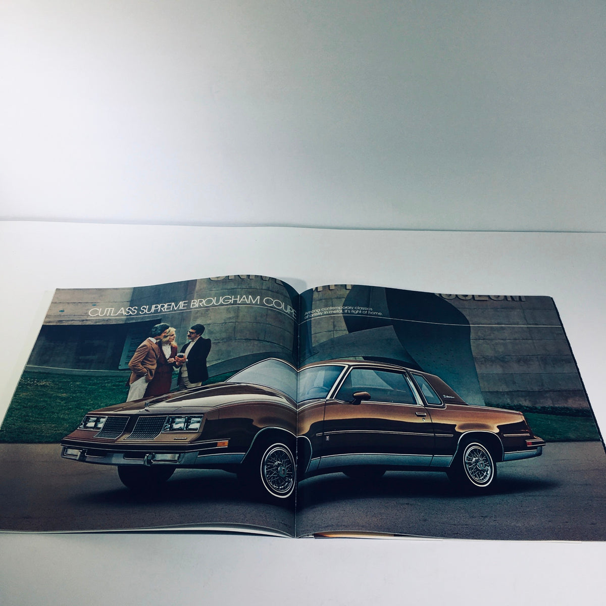 Spread from the 1983 Oldsmobile Cutlass Ciera, Supreme & Cruiser (110 Cid) L4 EFI Car Brochure featuring the Cutlass Supreme Brougham Coupe with people in a refined setting.