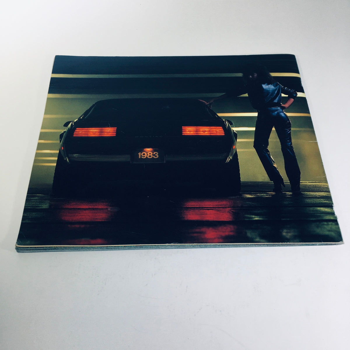 Rear view of a 1983 Pontiac car with illuminated taillights, captured in a garage, as part of the 1983 Pontiac 2000 5.8 Liter V-8 Engine Grand Prix Car Sale Brochure.
