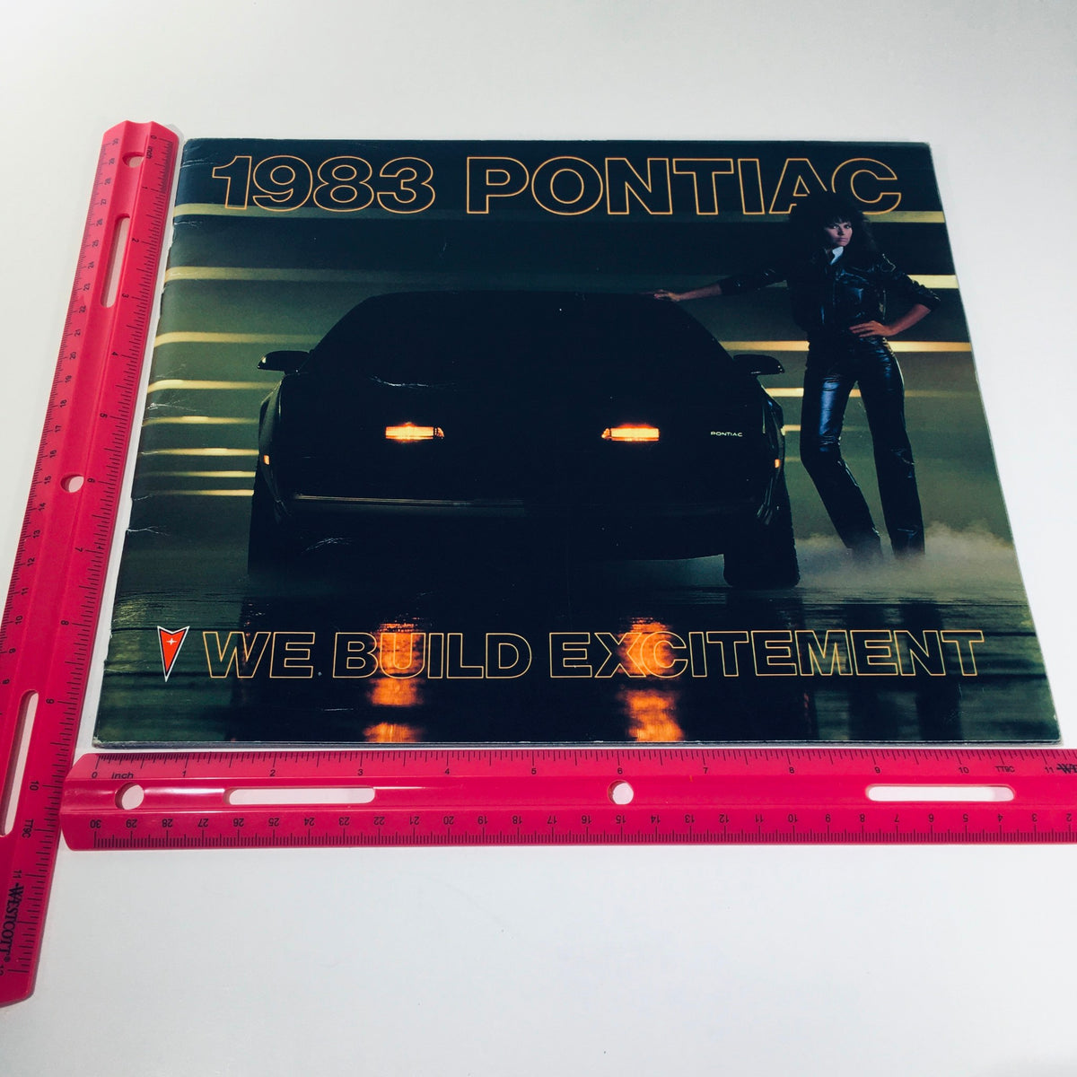 Cover image of the 1983 Pontiac 2000 5.8 Liter V-8 Engine Grand Prix Car Sale Brochure featuring a Pontiac car and a model, highlighting the theme "We Build Excitement."