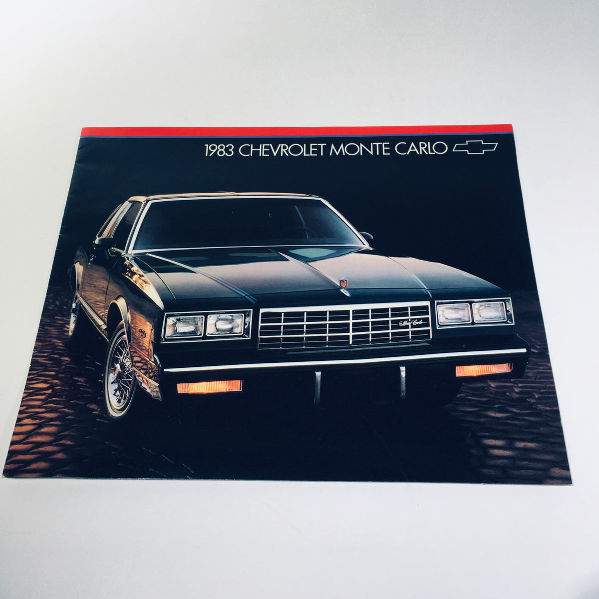 1983 Chevrolet Monte Carlo V6 or V8 Engine Full Coil Suspension Car Brochure front cover featuring a sleek black Monte Carlo against a dark background.